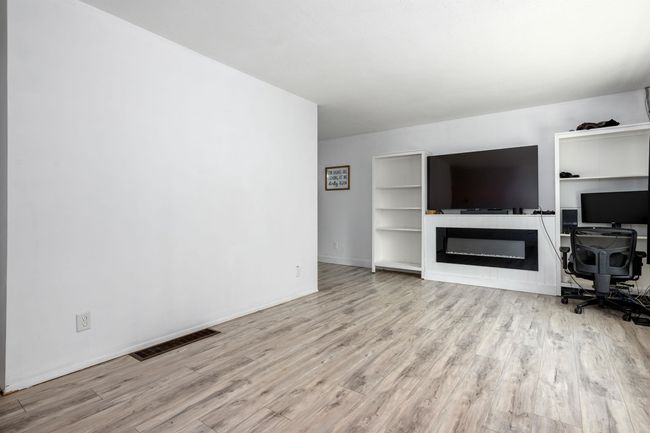Unfurnished living room featuring wood finished floors, a desk, a glass covered fireplace, and baseboards | Image 12