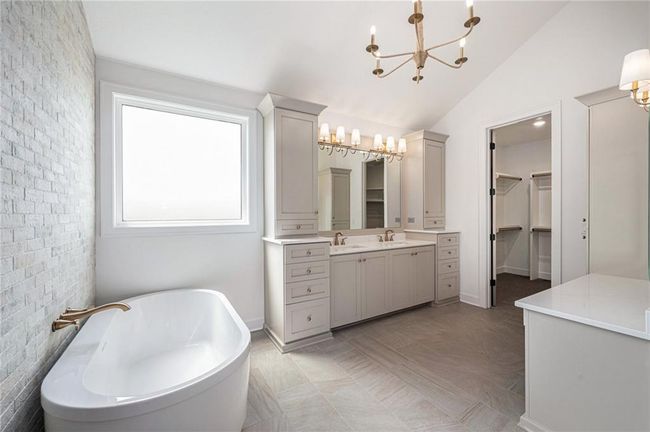 Full bathroom featuring a chandelier, vanity, a freestanding tub, a spacious closet, and lofted ceiling | Image 35
