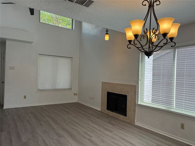 Unfurnished living room featuring wood finished floors, a textured ceiling, a chandelier, baseboards, and visible vents | Image 10