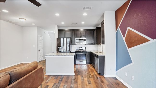 Kitchen with a center island, hardwood / wood-style flooring, appliances with stainless steel finishes, light stone countertops, and visible vents | Image 12