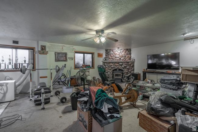 Exercise area featuring a textured ceiling, a ceiling fan, carpet flooring, and a glass covered fireplace | Image 49