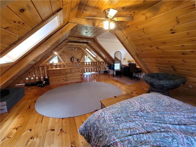 Bedroom featuring ceiling fan, hardwood / wood-style floors, vaulted ceiling with skylight, wood ceiling, and wooden walls | Image 8