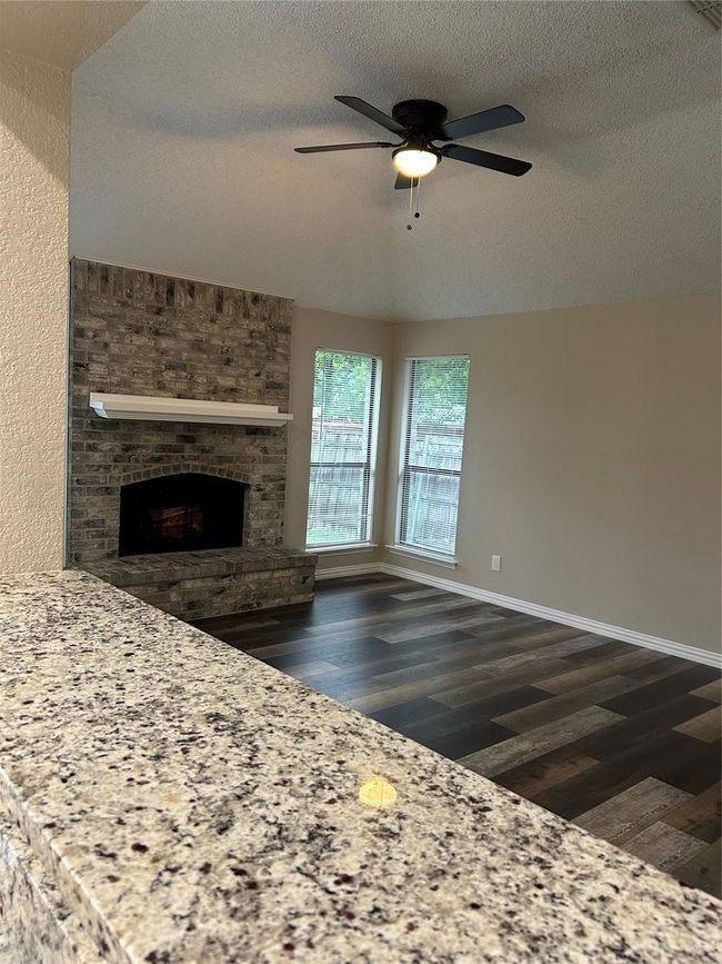 Unfurnished living room featuring dark wood finished floors, a textured ceiling, a brick fireplace, and a ceiling fan | Image 4