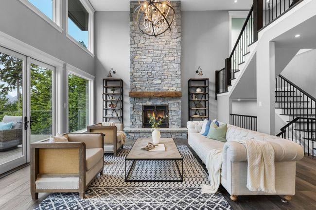 Living area featuring a high ceiling, wood finished floors, stairway, a chandelier, and a fireplace | Image 8