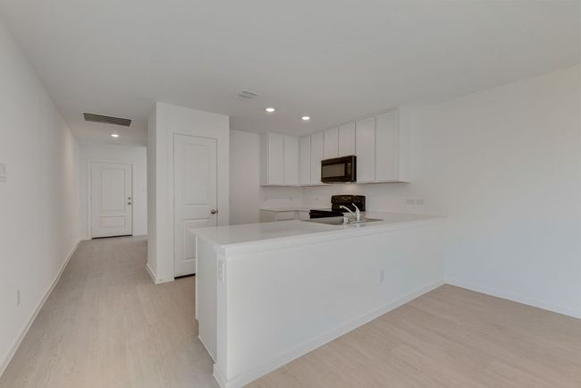 Kitchen featuring white cabinets, a peninsula, black appliances, light wood-style flooring, and recessed lighting | Image 9