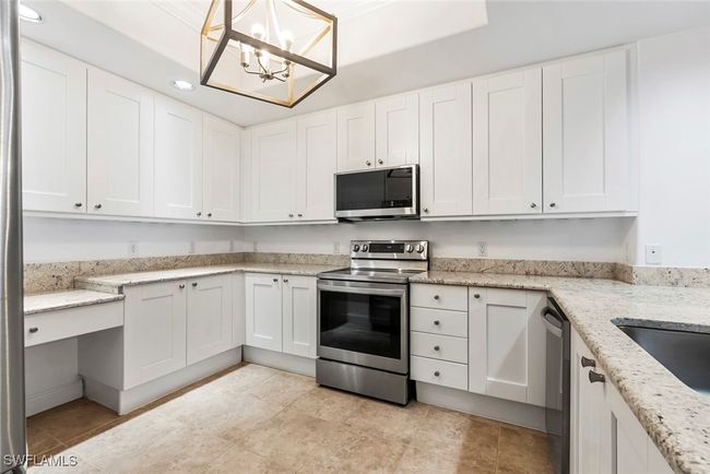 Kitchen with appliances with stainless steel finishes, white cabinetry, pendant lighting, light stone counters, and a chandelier | Image 31