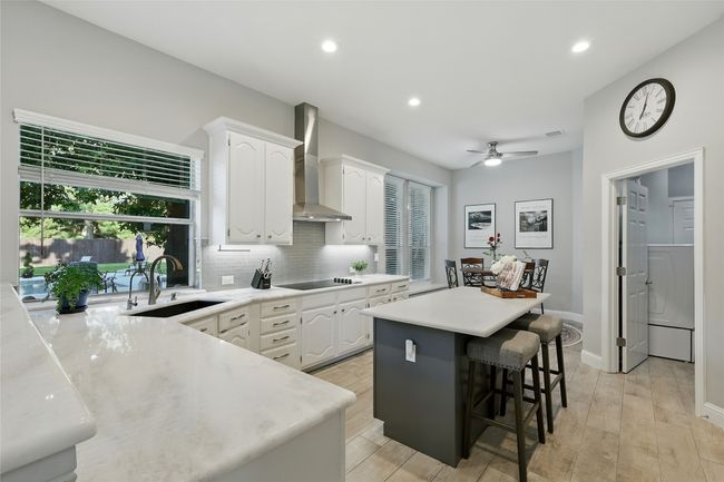 Kitchen featuring natural stone countertops, wall chimney range hood, white cabinets, black electric cooktop, a center island, and recessed lighting | Image 11