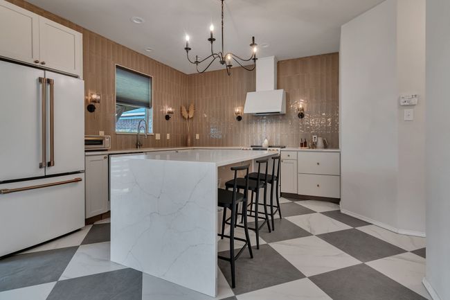 Kitchen with high end white fridge, wall chimney exhaust hood, a chandelier, a center island, and decorative backsplash | Image 13