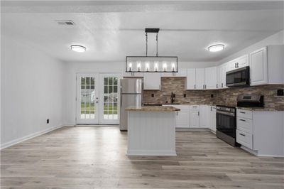 Kitchen featuring light wood-type flooring, appliances with stainless steel finishes, white cabinetry, a kitchen island, and tasteful backsplash | Image 2