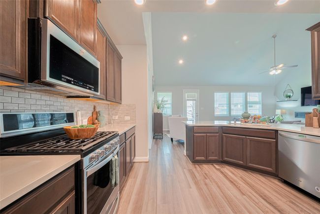This modern kitchen features sleek dark cabinets, stainless steel appliances, and a spacious open layout leading into a bright living area with large windows and high ceilings. Perfect for entertaining. | Image 17
