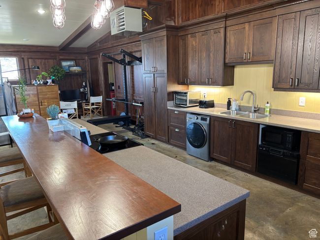 Kitchen featuring dark brown cabinets, washer / dryer, sink, and black microwave | Image 61