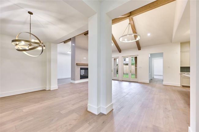 This photo showcases a spacious open-concept living area with elegant light fixtures, large windows, and exposed wooden beams. The room features engineered white oak floors and a modern fireplace, creating a warm and inviting atmosphere. | Image 9