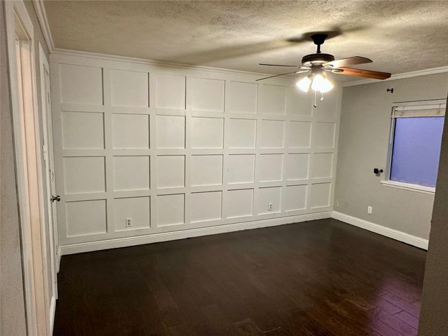 Primrary room with ornamental molding, dark wood-style floors, a ceiling fan, a textured ceiling, and a decorative wall | Image 22