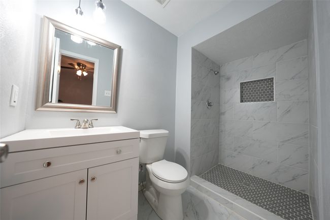 Full bathroom featuring ceiling fan, toilet, vanity, marble finish floor, and tiled shower | Image 15