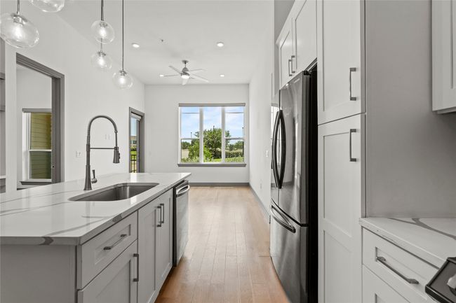 Kitchen with stainless steel appliances, a sink, light wood-style flooring, a ceiling fan, and a center island with sink | Image 25