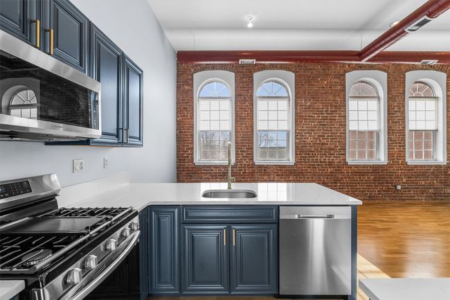 Kitchen featuring light countertops, appliances with stainless steel finishes, a sink, brick wall, and blue cabinets | Image 13