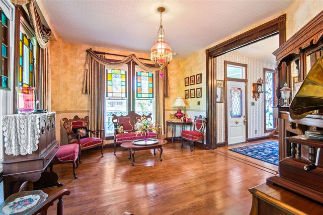 Living area featuring a chandelier, a wainscoted wall, wallpapered walls, wood finished floors, and pocket doors. | Image 5