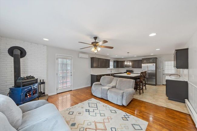 Living area featuring a baseboard radiator, a wall unit AC, light wood finished floors, and ceiling fan | Image 39
