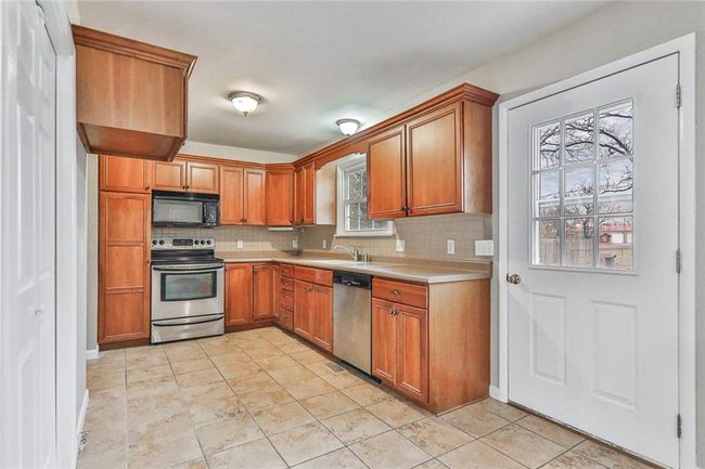 Kitchen featuring backsplash, sink, light tile patterned flooring, and appliances with stainless steel finishes | Image 4