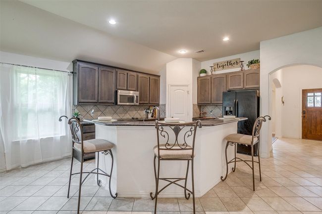 Kitchen with stainless steel microwave, arched walkways, black fridge, dark countertops, and a breakfast bar area | Image 12