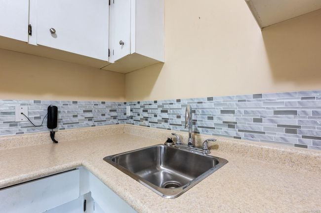 Kitchen view of a sink, white cabinets, backsplash, and light countertops | Image 24