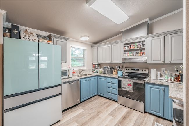 Kitchen featuring stainless steel appliances, ornamental molding, vaulted ceiling, blue cabinets, and light wood-style floors | Image 9