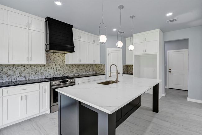 Kitchen featuring stainless steel range with gas cooktop, light stone counters, ventilation hood, tasteful backsplash, and a center island with sink | Image 14