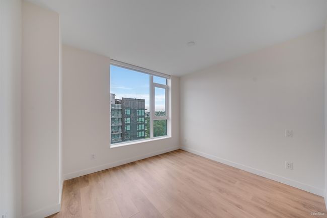 Empty room featuring light wood finished floors, baseboards, and a city view | Image 7