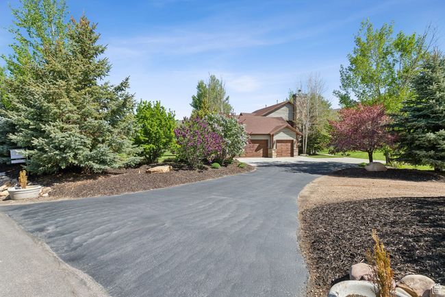 View of property hidden behind natural elements with driveway, brick siding, and an attached garage | Image 56