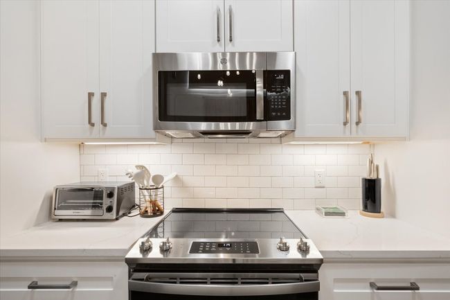 Kitchen featuring stainless steel appliances, white cabinets, tasteful backsplash, and light stone countertops | Image 9