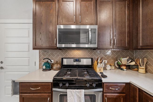 Kitchen with light countertops, dark brown cabinetry, appliances with stainless steel finishes, and decorative backsplash | Image 11