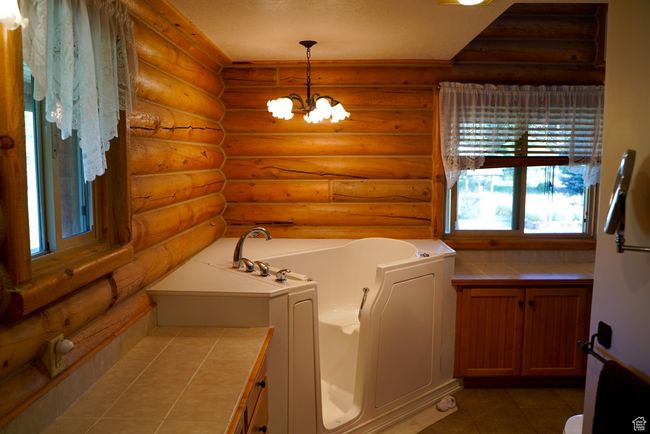 Bathroom with a bath, rustic walls, a chandelier, and tile patterned flooring | Image 12