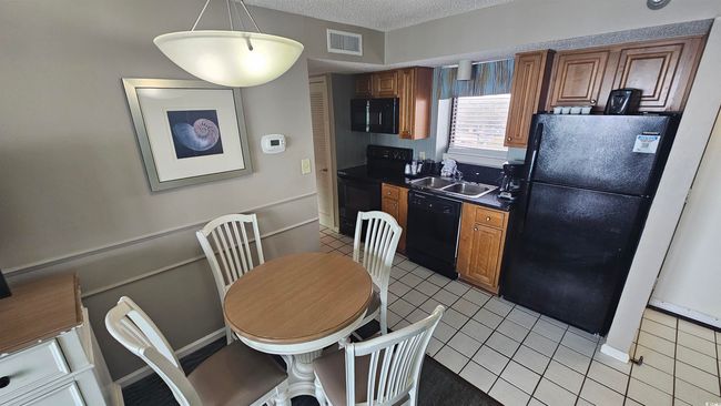 Kitchen featuring light tile patterned floors, a textured ceiling, a sink, visible vents, and black appliances | Image 4