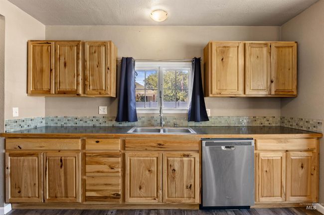 Kitchen with stainless steel dishwasher, a textured ceiling, dark countertops, decorative backsplash, and dark wood finished floors | Image 17