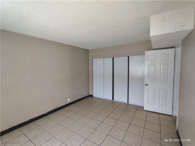 Unfurnished bedroom with concrete block wall, a textured ceiling, and a closet | Image 9