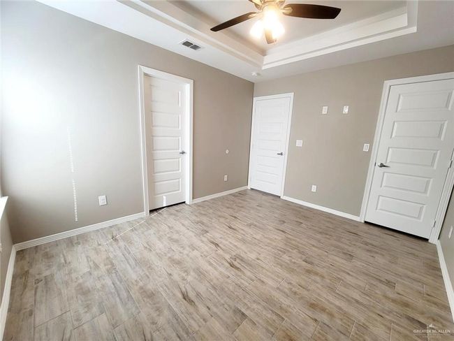 Unfurnished bedroom featuring a tray ceiling, light wood finished floors, and a ceiling fan | Image 13