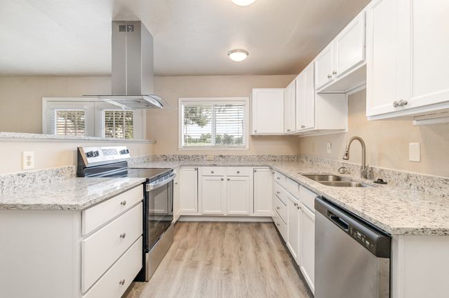 Kitchen featuring appliances with stainless steel finishes, island range hood, white cabinets, and light stone counters | Image 12