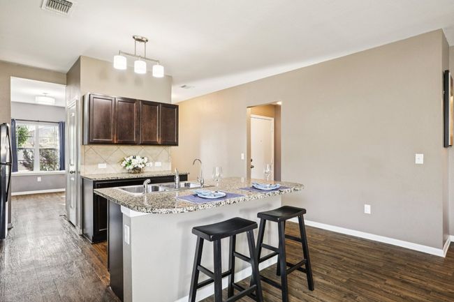 Kitchen with dark wood finished floors, dark brown cabinets, an island with sink, a breakfast bar area, and tasteful backsplash | Image 10