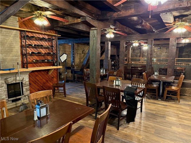 Dining space featuring a ceiling fan, wood finished floors, a stone fireplace, and beam ceiling | Image 32