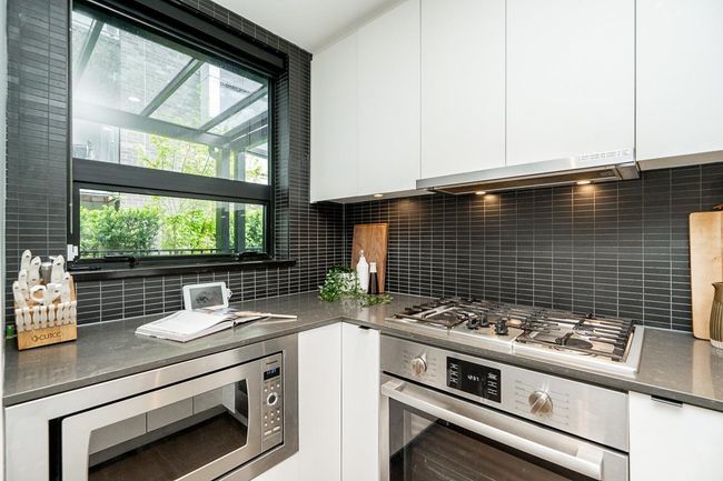 Kitchen with stainless steel appliances, white cabinets, modern cabinets, dark countertops, and range hood | Image 6
