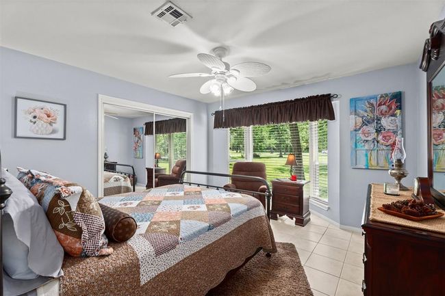 Bright bedroom with large windows offering garden views. Features include a ceiling fan, tiled floors, and a mirrored closet. | Image 16