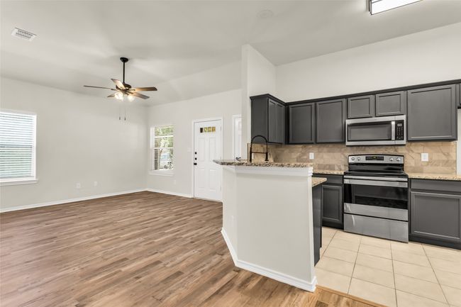 Kitchen featuring decorative backsplash, stainless steel appliances, light wood-style flooring, light stone countertops, and a ceiling fan | Image 7