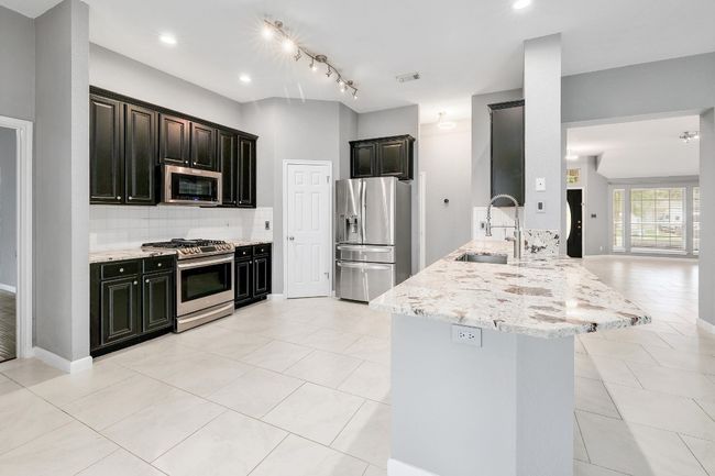 Kitchen featuring a sink, a peninsula, stainless steel appliances, backsplash, and light stone counters | Image 12