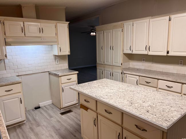 Kitchen with light countertops, decorative backsplash, a ceiling fan, light wood-style floors, and under cabinet range hood | Image 8