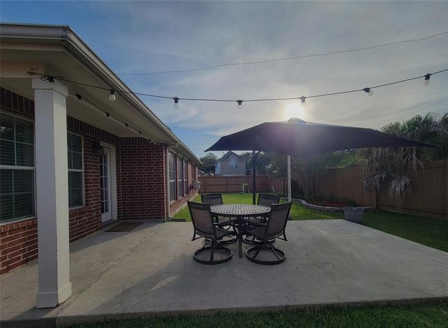 This photo showcases a cozy backyard patio with a large umbrella and seating area on a concrete slab, surrounded by a grassy lawn and a wooden fence. The brick exterior of the home adds a classic touch, and string lights provide charming ambiance. Perfect for outdoor entertaining. | Image 30