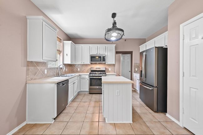 Kitchen featuring appliances with stainless steel finishes, decorative backsplash, white cabinetry, light countertops, and a center island | Image 12