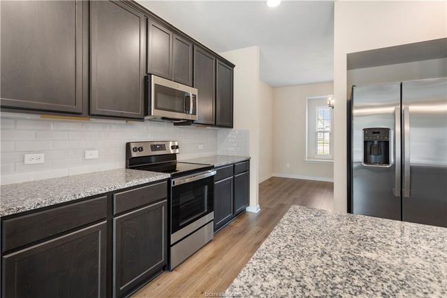 Kitchen featuring appliances with stainless steel finishes, light wood-style floors, backsplash, light stone countertops, and dark brown cabinets | Image 9