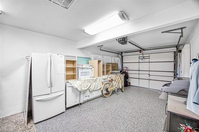 Garage featuring a garage door opener, visible vents, and freestanding refrigerator | Image 40