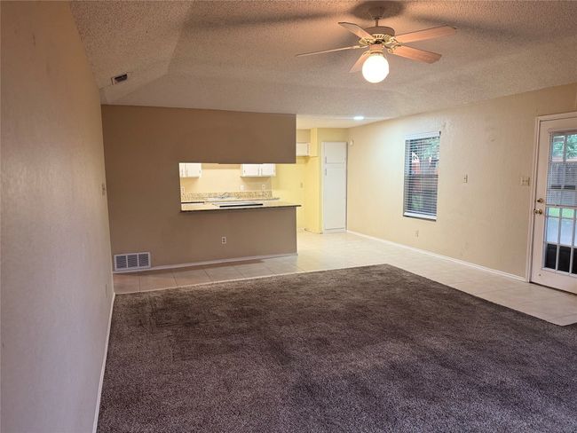 Unfurnished living room with a ceiling fan, a textured ceiling, light tile patterned floors, and visible vents | Image 6