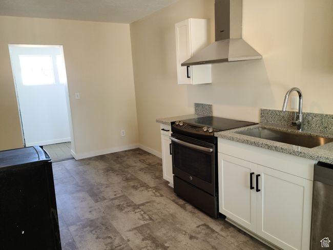Kitchen featuring wall chimney exhaust hood, electric range, a sink, dishwasher, and white cabinets | Image 11
